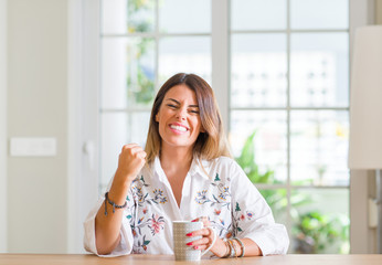 Young woman at home drinking coffee annoyed and frustrated shouting with anger, crazy and yelling with raised hand, anger concept