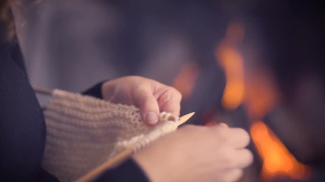 Woman hands knitting on winter fireplace background