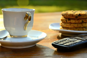 Morning espresso with oatmeal cookies, telephone, teaspoon, saucer, outdoors.