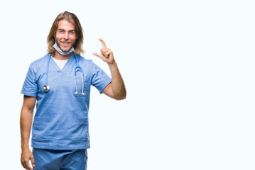 Young handsome doctor man with long hair over isolated background smiling and confident gesturing with hand doing size sign with fingers while looking and the camera. Measure concept.