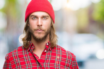 Young handsome man with long hair wearing red cap over isolated background with serious expression on face. Simple and natural looking at the camera.