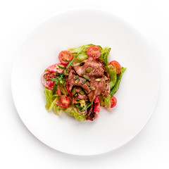 Delicious green meat salad with roasted juicy steak, tomato and green sauce in a white plate isolated on white background. Top view, flat lay