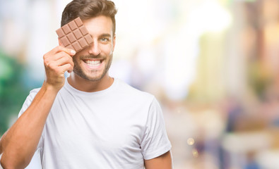 Young handsome man eating chocolate bar over isolated background with a happy face standing and...