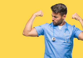 Young handsome doctor surgeon man over isolated background showing arms muscles smiling proud....