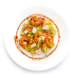 Seafood Caesar salad with prawns, rocket leaves, cherry tomatoes and parmesan cheese on a round white plate. Light background and top view .
