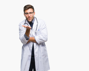 Young handsome doctor man over isolated background looking at the camera blowing a kiss with hand on air being lovely and sexy. Love expression.