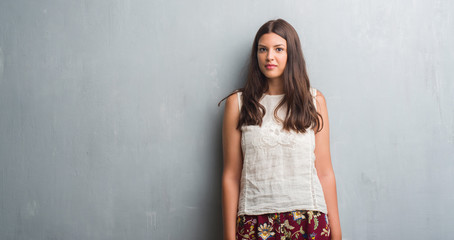 Young brunette woman over grunge grey wall with a confident expression on smart face thinking serious