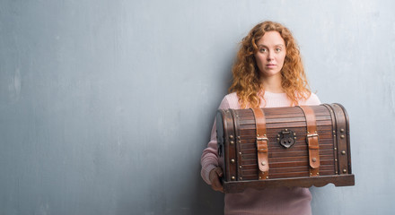 Young redhead woman holding vintage chest with a confident expression on smart face thinking serious