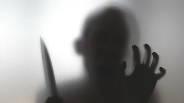 Man with knife behind frosted glass in 4k slow motion 60fps