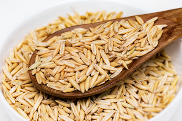 Wooden spoon with unpeeled oats at bowl isolated at white background.