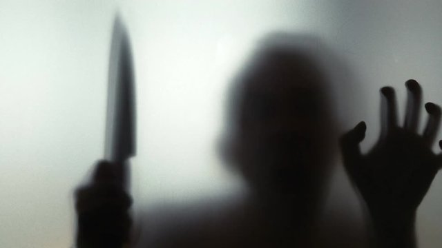 Man with knife behind frosted glass in 4k slow motion 60fps