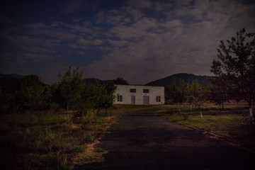 Mountain night landscape of building at forest at night with moon or vintage country house at night with clouds and stars. Summer night.