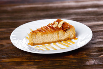 Closeup slice of cheesecake decorated with maple syrup at wooden board background.