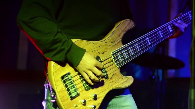 Close-up of a man playing bass guitar in a band. Musician playing a bass guitar on stage at concert. Young electric bass guitar player playing with hands 