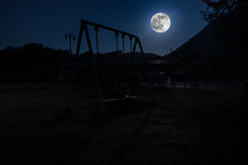 Night photo of metal swing standing outdoor at night with Moon. Nobody there.