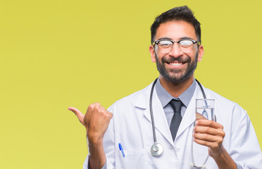 Adult hispanic doctor man drinking glass of water over isolated background pointing and showing with thumb up to the side with happy face smiling