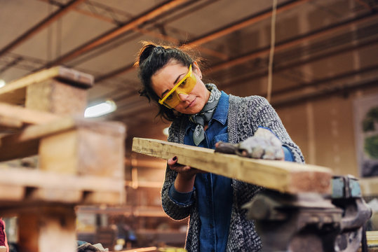 Picture of middle age focused female carpenter looking and choosing wood for her work in a workshop.