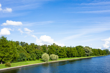 Green shore of the park, embankment of the river. Sky with clouds