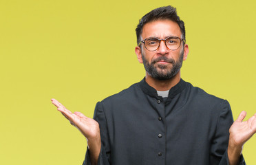 Adult hispanic catholic priest man over isolated background clueless and confused expression with...