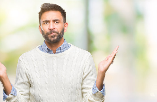 Adult hispanic man wearing winter sweater over isolated background clueless and confused expression with arms and hands raised. Doubt concept.