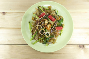 Thai food, fried noodle with seafood in soy sauced and vegetable  in a green plate on wooden floor background ,Top view Copy Space.