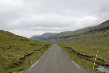 Straight mountain road running towards the distant mountains hiding in clouds.