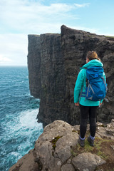 Unrecognizable hiker girl stands on edge of cliff and watches the raging ocean.