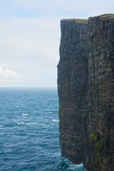 AERIAL: Flying above the blue ocean and towards a breathtaking rocky cliff.