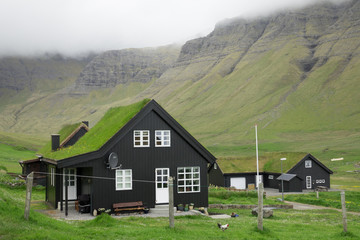 Remote village with black houses lies in vast green valley under the mountains.