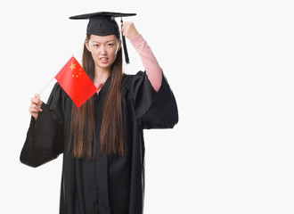 Young Chinese woman wearing graduate uniform holding China flag annoyed and frustrated shouting with anger, crazy and yelling with raised hand, anger concept