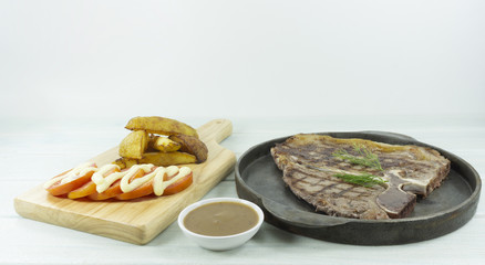Grilled T-bone beef steak on white wood floor background props decoration Chopping Wood board with potatoes and Gravy Sauce,Top view with copy space for your text..