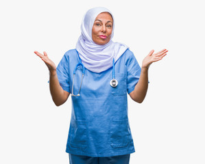 Middle age senior arab nurse woman wearing hijab over isolated background clueless and confused expression with arms and hands raised. Doubt concept.