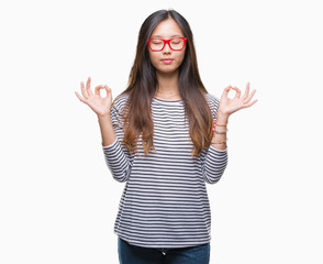 Young asian woman wearing glasses over isolated background relax and smiling with eyes closed doing meditation gesture with fingers. Yoga concept.