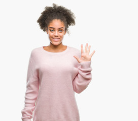 Young afro american woman wearing winter sweater over isolated background showing and pointing up with fingers number five while smiling confident and happy.