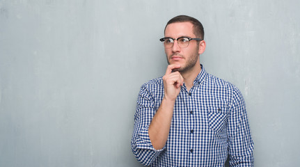 Young caucasian business man over grey grunge wall serious face thinking about question, very confused idea