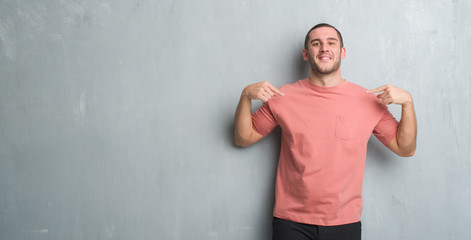 Young caucasian man over grey grunge wall looking confident with smile on face, pointing oneself with fingers proud and happy.