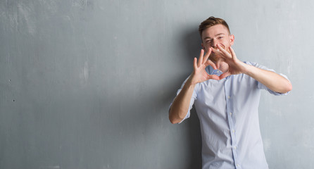 Young redhead business man over grey grunge wall smiling in love showing heart symbol and shape with hands. Romantic concept.