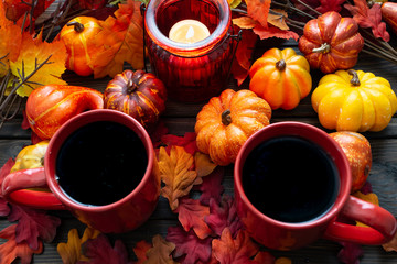 Autumn setting with small pumpkins and a red candle holder emitting light on two cups of morning coffee