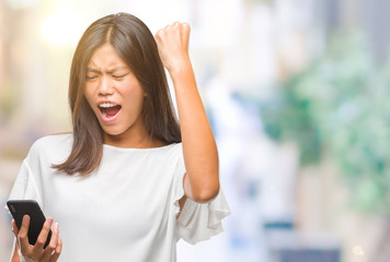 Young asian woman texting using smartphone over isolated background annoyed and frustrated shouting with anger, crazy and yelling with raised hand, anger concept