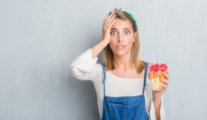 Beautiful young woman over grunge grey wall eating fruits stressed with hand on head, shocked with shame and surprise face, angry and frustrated. Fear and upset for mistake.