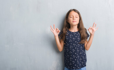 Young hispanic kid over grunge grey wall relax and smiling with eyes closed doing meditation gesture with fingers. Yoga concept.