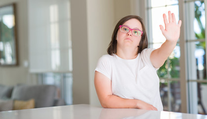Down syndrome woman at home with open hand doing stop sign with serious and confident expression, defense gesture