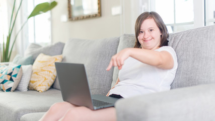Obraz na płótnie Canvas Down syndrome woman at home using computer laptop very happy pointing with hand and finger