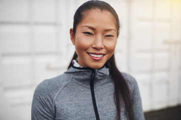 Smiling young Asian woman in sportswear standing outside