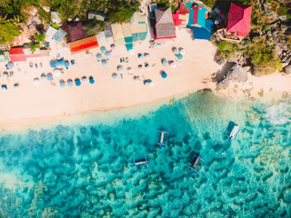 Aerial view of sandy beach with turquoise sea water and local tradition boats, drone shot