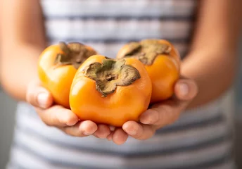 Crédence de cuisine en verre imprimé Fruits Hand holding persimmon fruit for giving
