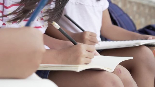 Asian little pupil draw in notebooks on their knees during an outdoor class at summer camp. Concept of learning and lifestyle in teens life.
