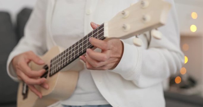 Woman play a song on ukulele at home