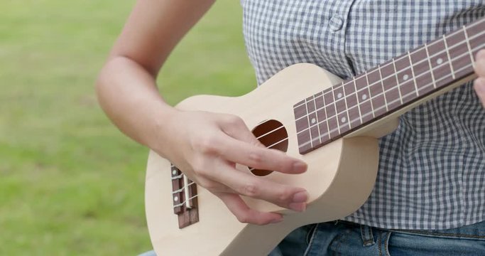 Woman play ukulele and sitting on the grass