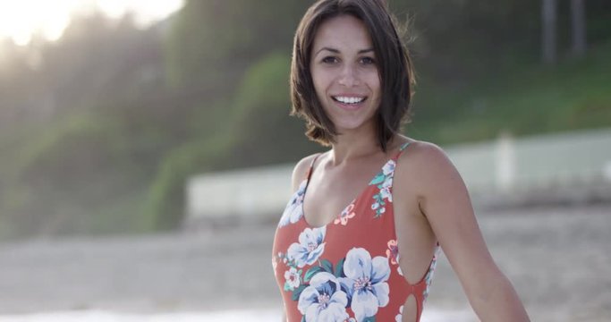 Beautiful hip young woman in one piece bathing suit walking backwards on beach - rack focus